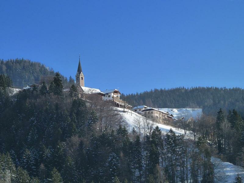 Verschneites Laurein mit Kirchturm und Wald im Winter